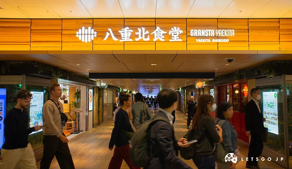 「八重北食堂」美食街入口,木質招牌橫跨通道上方,許多行人正在通過。